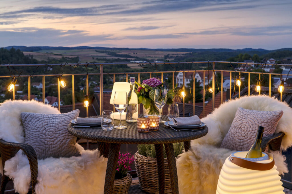 Gemütlich hergerichtete Sitzplätze mit Tisch auf einem Balkon am Abend.